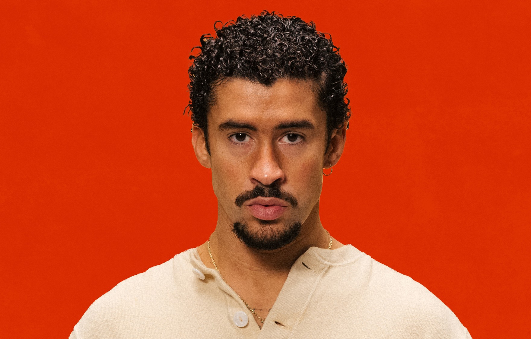 Prévu en concert à Paris et Marseille en 2026, le chanteur Bad Bunny prend la pose sur un fond rouge.