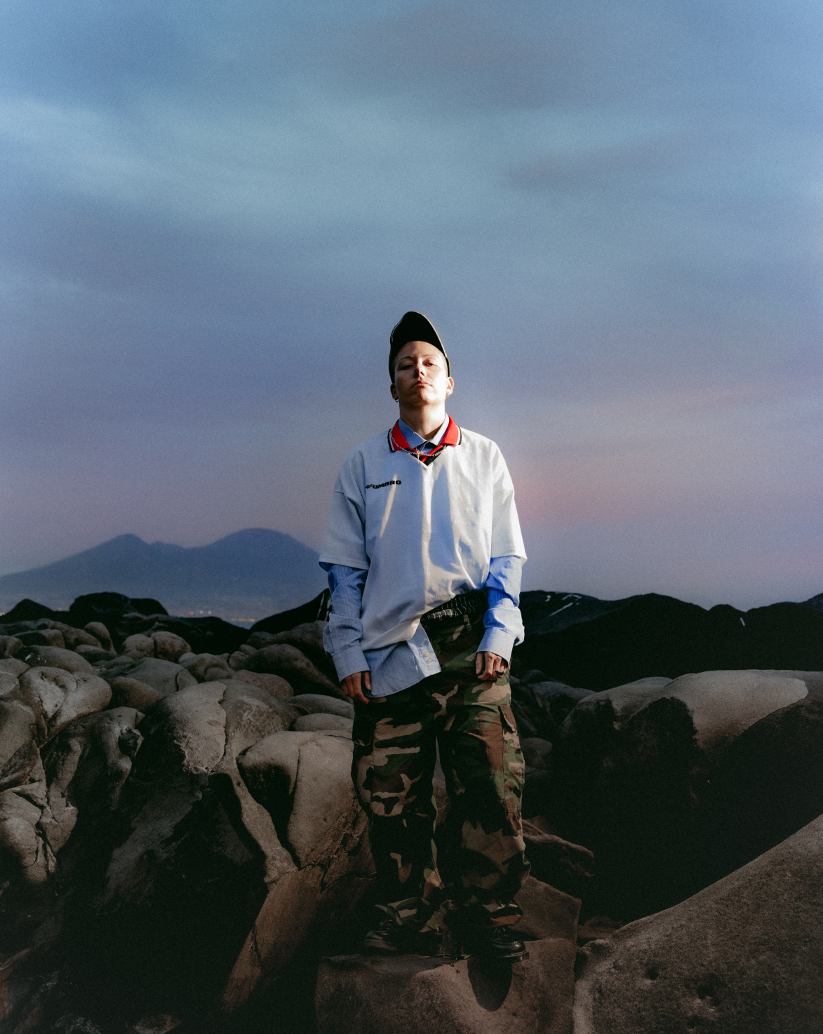 Nziria pose au milieu de rochers dans un polo blanc.